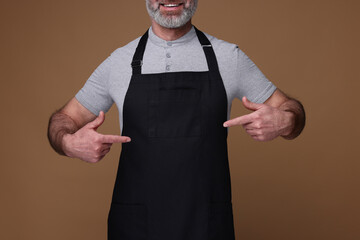 Man pointing at kitchen apron on brown background, closeup. Mockup for design