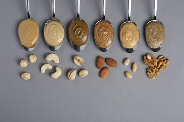 Fotobehang Tasty nut butters in spoons and raw nuts on gray table, flat lay. Space for text © New Africa