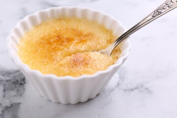 Delicious creme brulee in bowl and spoon on white marble table, closeup