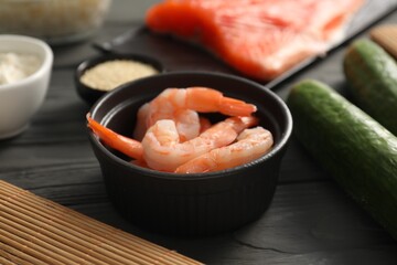 Fresh shrimps in bowl and other ingredients for sushi on black wooden table, closeup