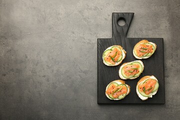 Tasty canapes with salmon, cucumber and cream cheese on grey table, top view. Space for text