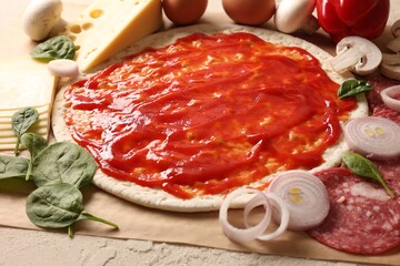 Pizza base smeared with tomato sauce and products on light textured table, closeup