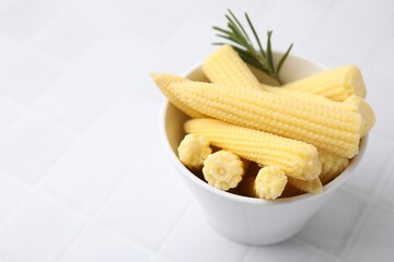 Tasty fresh yellow baby corns in bowl on white tiled table, closeup. Space for text
