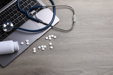 Laptop, stethoscope, pills and bottle on wooden table. Space for text