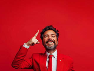 Obraz premium Elegant Man Red Suit Tie Pointing Up Confidence Red Background Copy Space&nbsp;