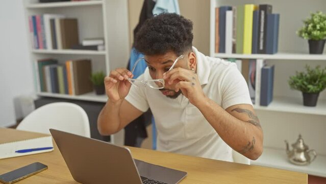 Young african american man sitting on table using laptop scared and amazed with open mouth for surprise, disbelief face at home