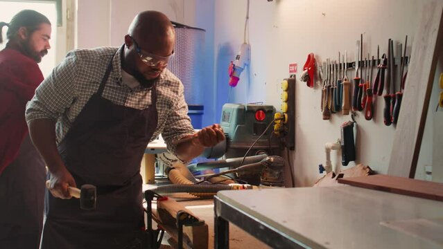 African american sculptor shaping raw timber using chisel and hammer in carpentry shop, creating wood art, wearing safety glasses. Artist making wood sculptures, engraving lumber with tools, camera B