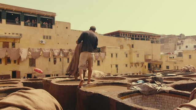 A Moroccan Worker Soaking Traditional Leather in the dye pool