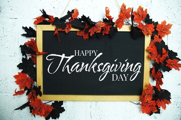 Happy Thanksgiving text message on Blackboard decoration with maple leaves hanging on a concrete...
