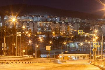 Night city landscape. View of the road to the city. Residential buildings in the distance. Bright light from street lamps. City of Tynda, Amur region, Siberia, Russia.