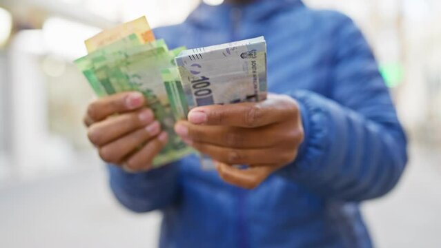 African woman holding south african rand in urban setting, depicting finance and economy.