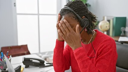 Stressed african american woman with headset in office touching head and looking down in frustration.