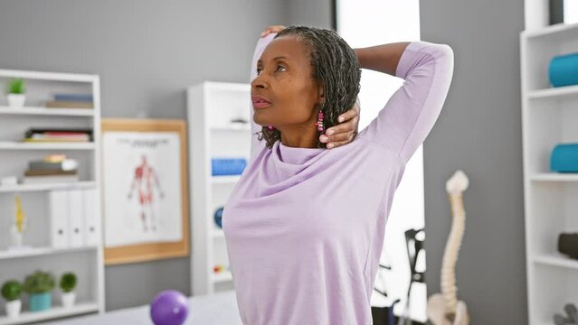 Mature african woman stretching arm in a physical therapy clinic interior