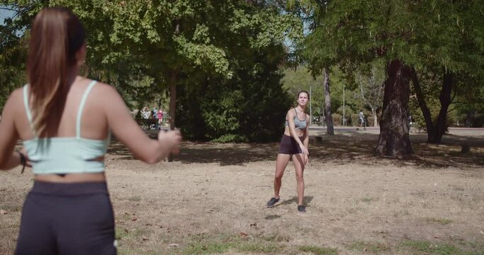 Two young women enjoying a friendly game of catch with a rugby ball in the park on a sunny day.