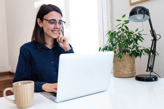 Happy young woman with glasses working with laptop at home. Vertical image. Copy space.