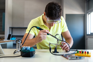 Caucasian male high school student in electronics class working on a project alone.