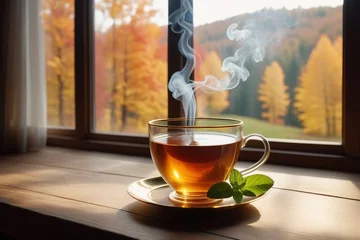 Poster A glass cup of hot tea with mint leaves on a wooden table beside a window, cozy background, horizontal composition © Thanh
