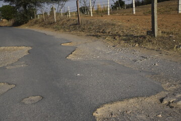 Bad road, cracked asphalt with potholes and big holes. Potholes on the road with stones on the asphalt. The asphalt surface is destroyed on the road. Bad condition of the road - 778663551