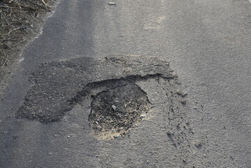 Bad road, cracked asphalt with potholes and big holes. Potholes on the road with stones on the asphalt. The asphalt surface is destroyed on the road. Bad condition of the road - 778663760