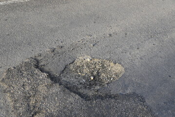 Bad road, cracked asphalt with potholes and big holes. Potholes on the road with stones on the asphalt. The asphalt surface is destroyed on the road. Bad condition of the road