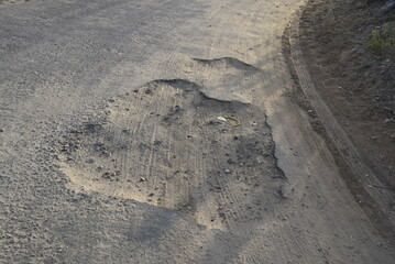 Bad road, cracked asphalt with potholes and big holes. Potholes on the road with stones on the asphalt. The asphalt surface is destroyed on the road. Bad condition of the road - 778663775