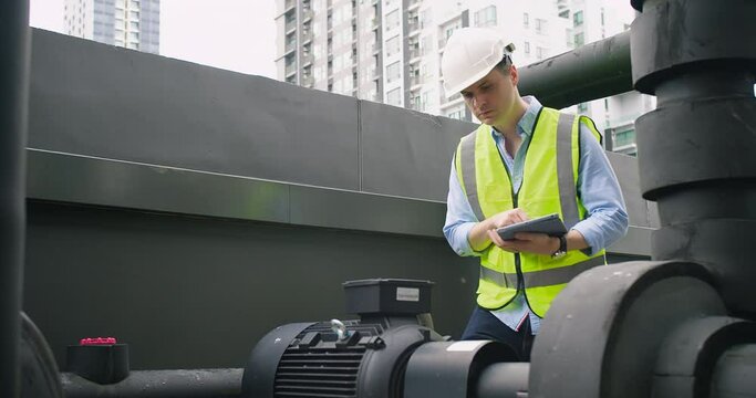 A Engineer man looking inspecting maintenance insulated pipelines valve pump control on the roof at an industrial site. He is wearing a hard hat and safety vest