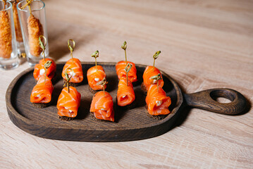 Salmon Roll Appetizers on Wooden Serving Board. Elegant smoked salmon rolls filled with cream cheese on dark rye bread, served on a rustic wooden board.