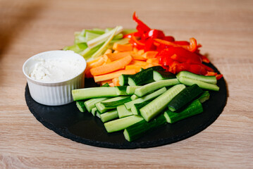 Fresh Cut Vegetable Sticks with Dip on Slate Board. Colorful assortment of fresh cut vegetables with a creamy dip, presented on a round slate serving board.