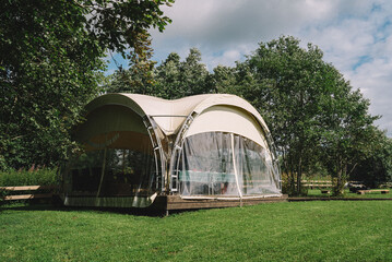 Modern Transparent Dome Amidst Lush Greenery. Eco-friendly transparent geodesic dome with a beige...
