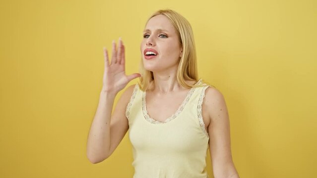 Blonde young woman wearing sleeveless t shirt standing clueless over yellow isolated background. arms open, baffled face, no idea, confused!