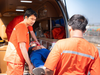 Paramedic in uniform  loading patient on stretcher into ambulanceworking together with team