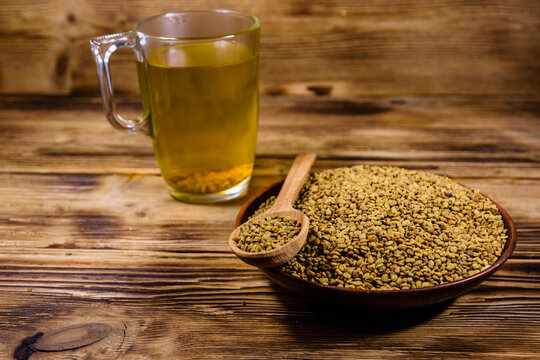 Cup of yellow tea (methi dana) and plate with fenugreek seeds on wooden table