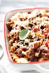 Baked pasta with cherry tomatoes, olives and mozzarella cheese. Bright wooden background. Close up.
