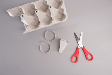 a pair of scissors sitting next to a egg carton box, pastel colors, red scissors, set pieces on grey surface