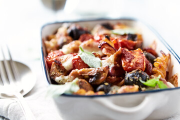 Baked pasta with cherry tomatoes, olives and mozzarella cheese. Bright wooden background. Close up.