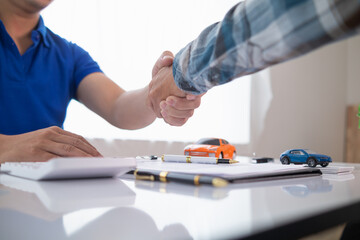 customer and car dealer shake hands after agreeing to sales contract before making contract payment...