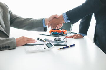 customer and car dealer shake hands after agreeing to sales contract before making contract payment...