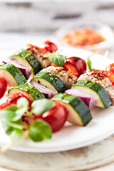 Grilled shashliks with vegetables and pork tenderloin. Bright wooden background. Close up.