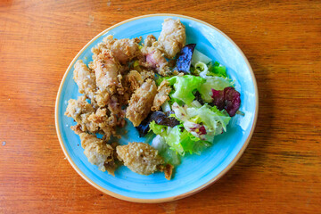 Crispy deep fried baby octopus served with salad on wooden table. Top view