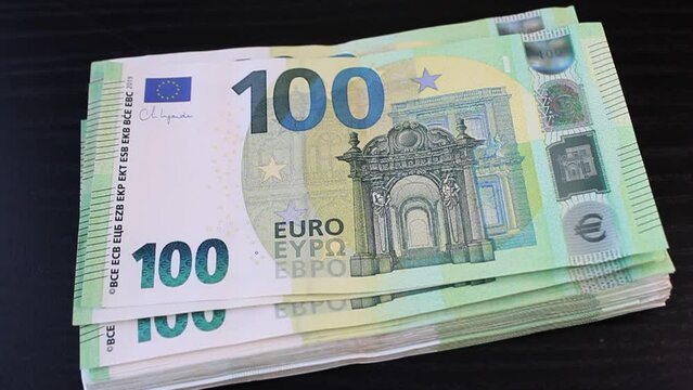 A stack of 100 euro banknotes falls freely on the surface of a black office desk
