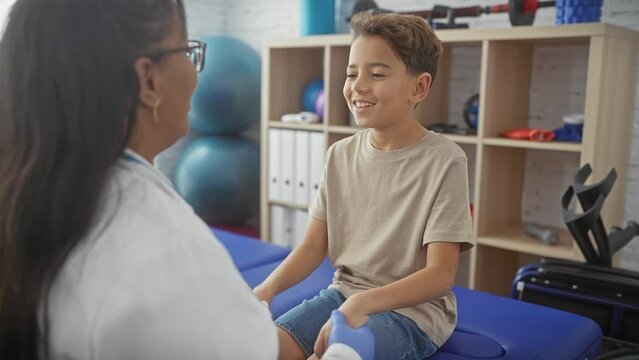 A smiling boy embracing a woman in a white coat indoors, depicting a warm moment between a child patient and a healthcare professional in a therapy room.