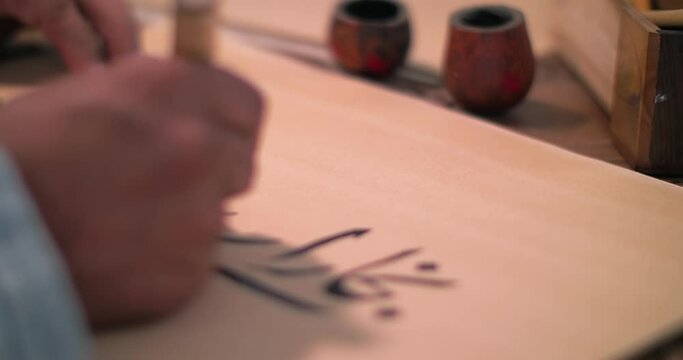 A calligrapher's hand dips a stylo into an inkwell and writes a letter on parchment