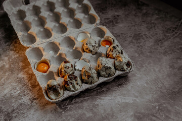 Cracked quail egg with broken shell in box on grey background