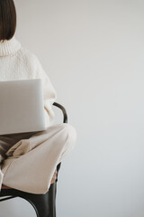 Woman in white pullover using laptop computer over white wall. Web, internet, social media online surfing. Neutral beige color