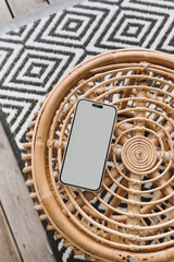 Naklejka premium Mobile phone with blank screen on ornamental wooden table and carpet. Flat lay, top view template with copy space