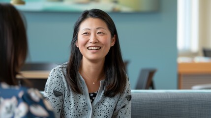 An Asian woman enjoys a relaxed conversation with a peer in a contemporary office lounge area