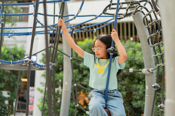 Obraz premium Joyful Asian girl having enjoy and fun playing on a zip line in an adventure park outdoors on the playground.