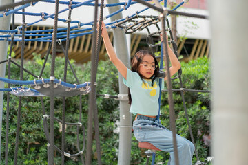 Fototapeta premium Joyful Asian girl having enjoy and fun playing on a zip line in an adventure park outdoors on the playground.