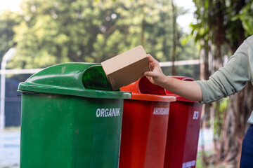 Hand throwing box into trash bin, waste disposal concept.