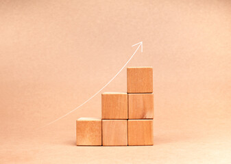 Rising up thin arrow on wooden cube blocks, minimalist bar graph chart steps on brown recycle paper background, profit, benefit, income, business growth process, trend, economic improvement concepts.